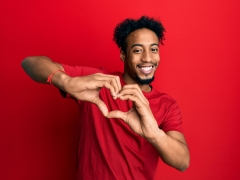  A young man wearing red and holding his hands in a heart shape. 