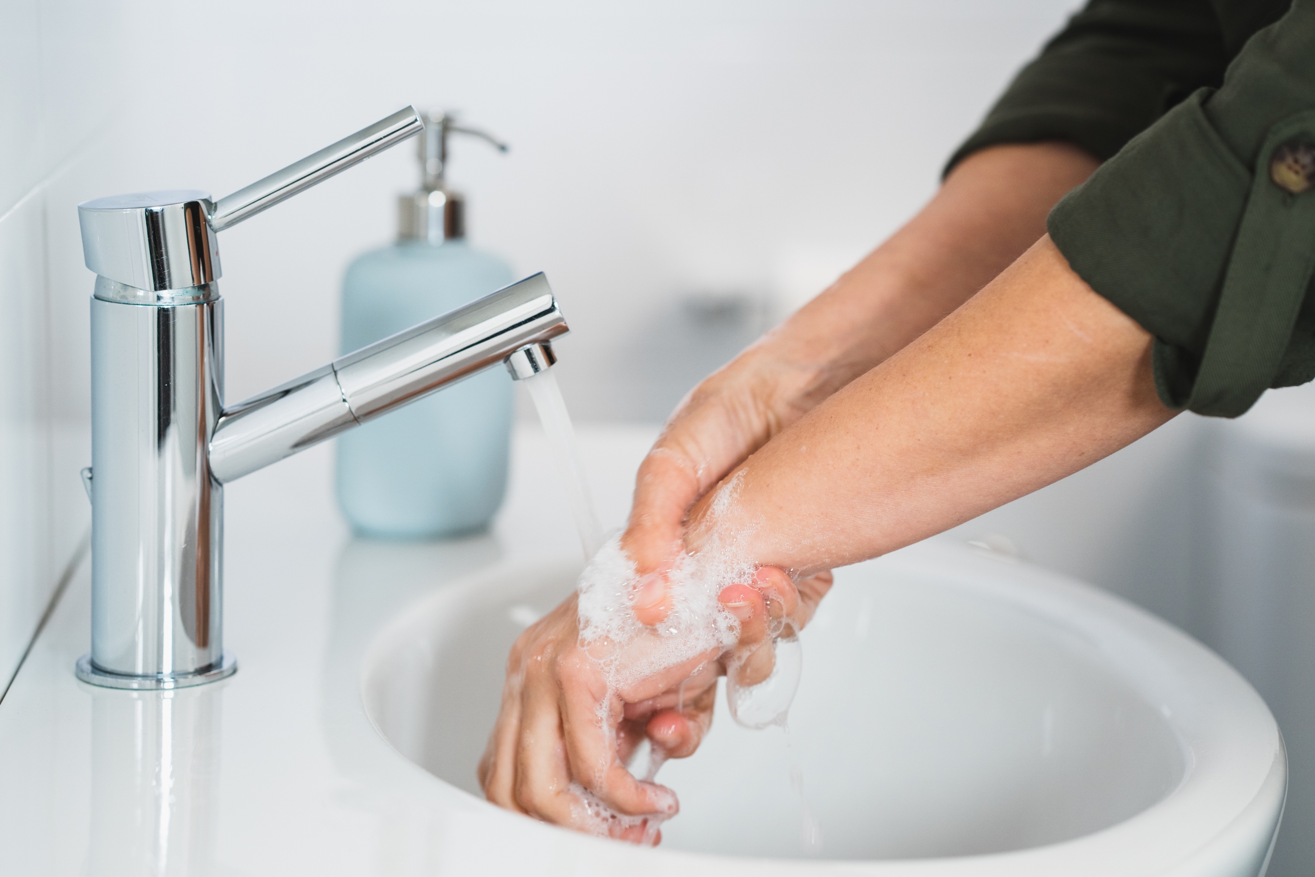 Young woman washing hands with soap over sink.